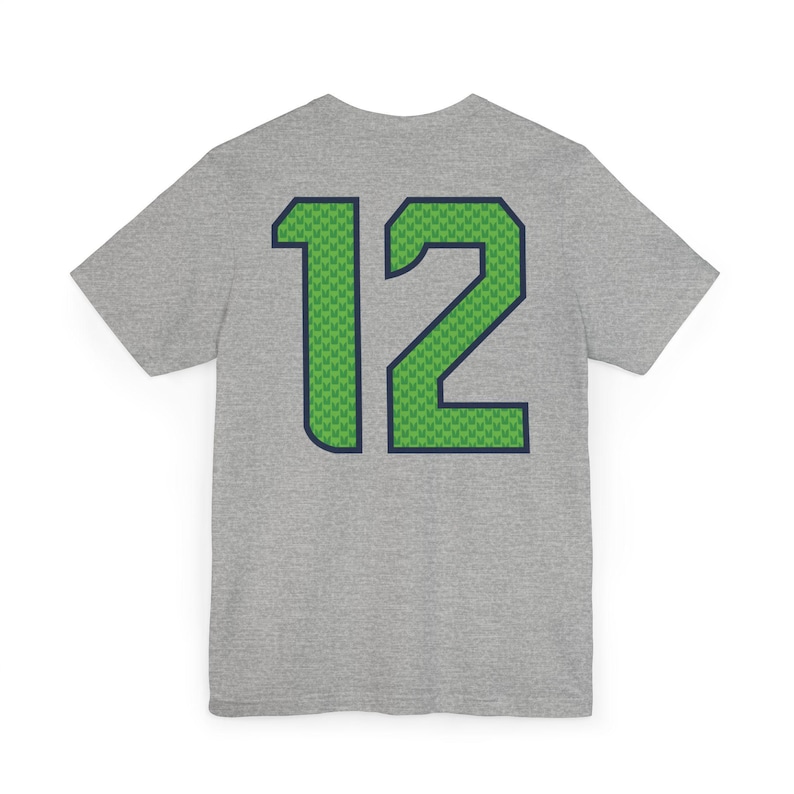 May include: A heather gray t-shirt with the number "12" on the back. The number is green with a blue outline and a green pattern fill. The shirt is short-sleeved and has a crew neck.