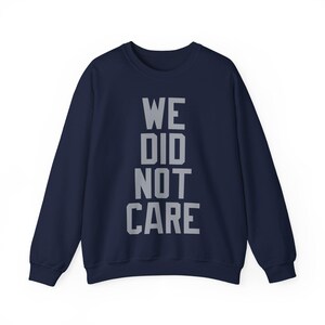May include: Navy blue sweatshirt with the text "WE DID NOT CARE" in gray block letters. The crew neck sweatshirt has long sleeves and a relaxed fit. The text is centered on the front of the garment.
