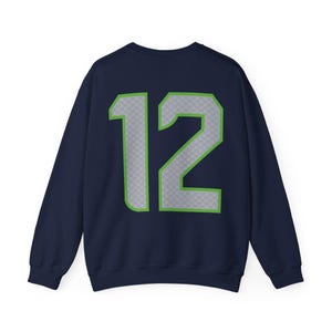 May include: Navy blue sweatshirt with the number 12 in gray with a green outline. The number has a subtle pattern. The sweatshirt is a crew neck style.