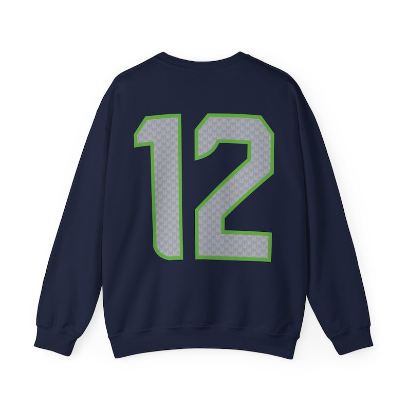 May include: Navy blue sweatshirt with the number 12 in gray with a green outline. The number has a subtle pattern. The sweatshirt is a crew neck style.