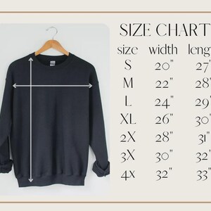 May include: A black sweatshirt hangs on a wooden hanger. The image includes a size chart with measurements in inches: S (20" width, 27" length), M (22" width, 28" length), L (24" width, 29" length), XL (26" width, 30" length), 2X (28" width, 31" length), 3X (30" width, 32" length), and 4X (32" width, 33" length).