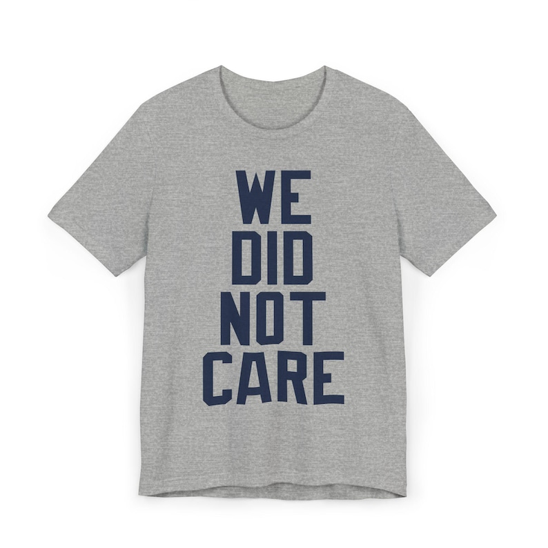 May include: A heather gray t-shirt with the navy blue text "WE DID NOT CARE" printed in a stacked format. The shirt has short sleeves and a crew neck.
