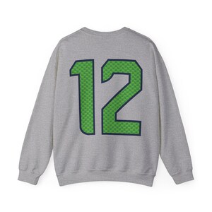 May include: A gray sweatshirt with the number "12" prominently displayed on the back. The number is green with a textured pattern and outlined in navy blue. The sweatshirt is a crew neck style.