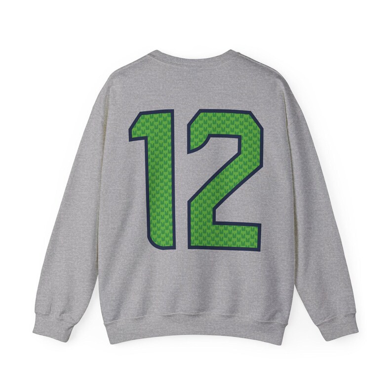 May include: A gray sweatshirt with the number "12" prominently displayed on the back. The number is green with a textured pattern and outlined in navy blue. The sweatshirt is a crew neck style.