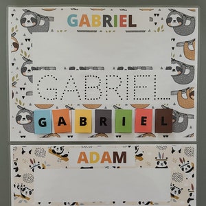 Può includere: Due pannelli di apprendimento colorati a tema bradipo e panda. I pannelli presentano i nomi "GABRIEL" e "ADAM" con linee tratteggiate per tracciare le lettere. Le lettere magnetiche vengono utilizzate per scrivere i nomi.