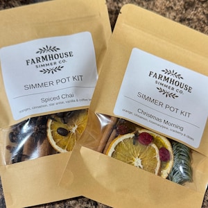 May include: Two brown paper pouches with clear windows, labeled "Farmhouse Simmer Co. Simmer Pot Kit." One is "Spiced Chai" with oranges, cinnamon, and star anise. The other is "Christmas Morning" with orange, cinnamon, and rosemary.