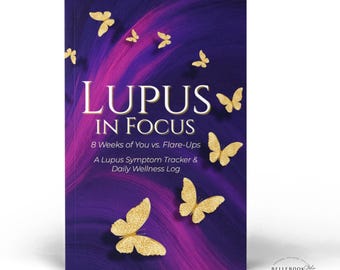 May include: A book titled "LUPUS IN FOCUS" with a purple and gold cover. The cover features gold butterflies and the text "LUPUS IN FOCUS" in large white letters. The book is a symptom tracker and daily wellness log.