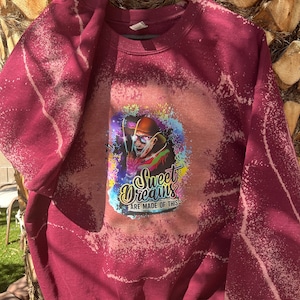 May include: Burgundy sweatshirt with a bleach-splattered design. The design features a cartoon character with sunglasses and a hat, holding a microphone. The text "Sweet Dreams Are Made Of This" is printed below the character.
