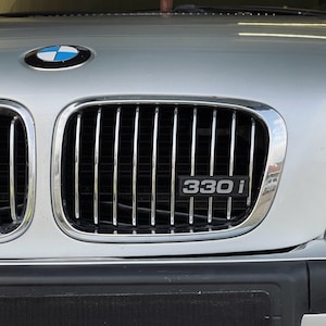 May include: A silver BMW 330i with a black grille and a blue and white BMW logo.