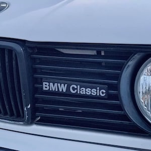 May include: Close-up of a white BMW car with a black grille and a silver "BMW Classic" emblem.