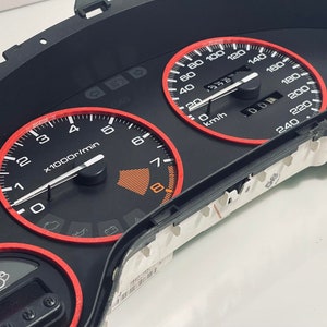 May include: A black car dashboard with red accents. The dashboard features a speedometer, tachometer, and other gauges. The speedometer reads up to 240 km/h and the tachometer reads up to 8,000 rpm.