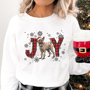 May include: White sweatshirt with the word "JOY" in a Christmas theme. The "J" and "Y" are red and black buffalo plaid. The "O" is a dog wearing a Santa hat and Christmas lights. Snowflakes surround the word.