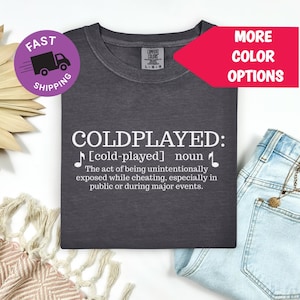 May include: Dark gray t-shirt with the word "COLDPLAYED" in white, along with a definition. A purple circle with a truck graphic and the words "FAST SHIPPING" is in the upper left. A red arrow points to "MORE COLOR OPTIONS".