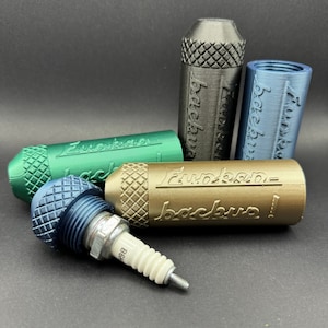 Può includere: Quattro piccoli contenitori cilindrici con una superficie testurizzata e la parola "backup!" in rilievo. I contenitori sono di diversi colori: nero, verde, blu e oro. Una candela è appoggiata sul tavolo accanto ai contenitori.