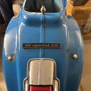 Può includere: Uno scooter Vespa blu con una luce posteriore cromata e una targa argentata che recita "50 special 2.0".
