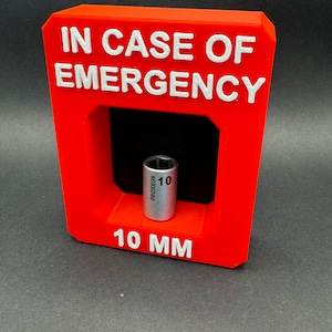 May include: Red plastic box with the text "IN CASE OF EMERGENCY" in white letters. The box has a cutout for a 10 mm socket, which is included. The socket is silver and has the text "PROXXON 10" on it.