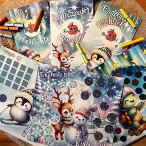 Könnte beinhalten: Eine Sammlung farbenfroher Kinderspielkarten mit winterlichen Illustrationen von Tieren wie Pinguinen, Rehen und einem Schneemann. Die Karten haben deutschen Text und werden von bunten Markern begleitet.