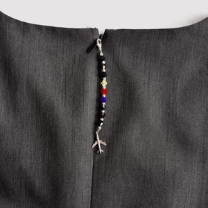 May include: A black zipper with a silver charm attached. The charm is a small airplane with a beaded chain of black, green, red, blue, and clear beads.
