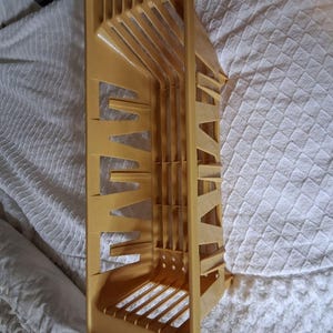 May include: A mustard-yellow plastic dish rack with a slotted design for drying plates and utensils. The rack has a rectangular base and angled supports, with multiple slots for holding dishes upright. The design allows for efficient air circulation.