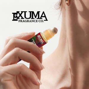 May include: A roll-on fragrance bottle held in a hand. The bottle has a colorful label with the text "EXUMA FRAGRANCE CO." The liquid inside is a light amber color. The bottle's applicator is a rollerball.