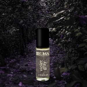 Puede incluir: Un frasco de perfume roll-on con tapa negra y etiqueta que dice "violet gray". El frasco es de 5 ml. Tambi&eacute;n se ve la marca "EXUMA FRAGRANCE CO.". El fondo es una escena de bosque oscura y borrosa.