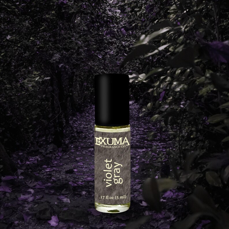 Puede incluir: Un frasco de perfume roll-on con tapa negra y etiqueta que dice "violet gray". El frasco es de 5 ml. Tambi&eacute;n se ve la marca "EXUMA FRAGRANCE CO.". El fondo es una escena de bosque oscura y borrosa.
