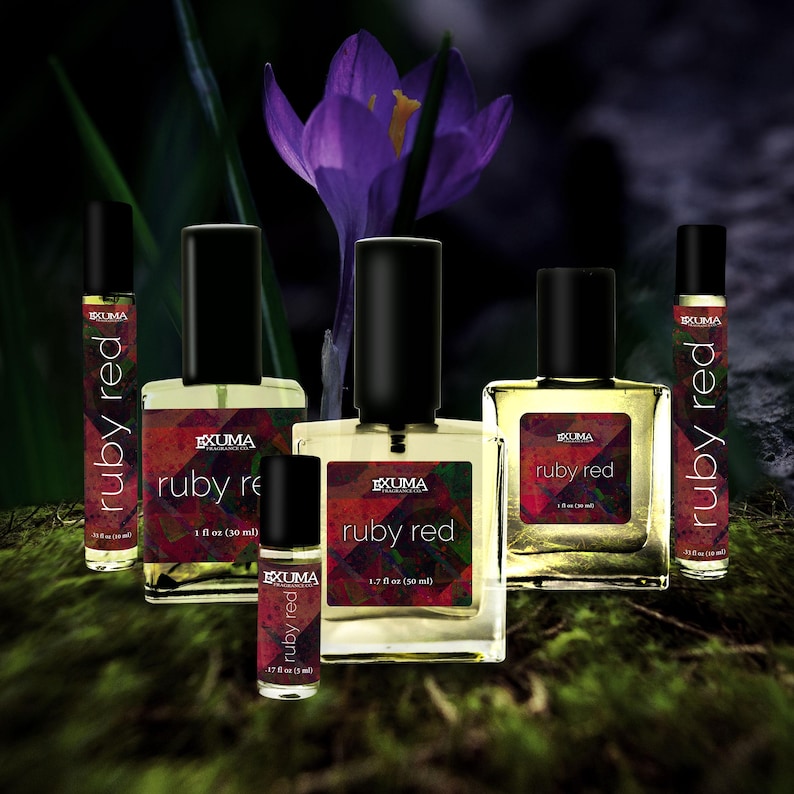 May include: An assortment of perfume bottles with black caps and labels that read "ruby red" in white text. The bottles vary in size, with the largest containing 1.7 fl oz (50 ml). A purple crocus flower is in the background.