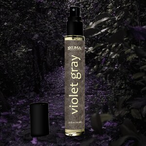 Puede incluir: Un frasco de perfume con tap&oacute;n negro y pulverizador. El frasco est&aacute; etiquetado "Violet Gray" con la marca "EXUMA" y contiene 10 ml. El fondo es una escena borrosa de un bosque con tonos morados.