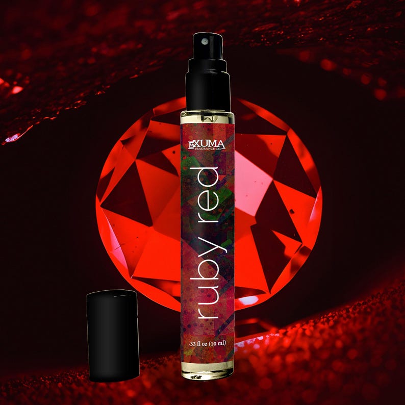 May include: A perfume bottle with a black cap and a spray nozzle. The bottle is labeled "ruby red" and contains 0.33 fl oz (10 ml) of liquid. The background features a large, faceted red gemstone.