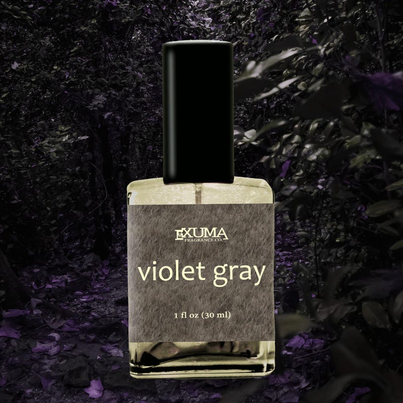 Puede incluir: Botella de perfume rectangular con tap&oacute;n negro. La etiqueta dice "EXUMA FRAGRANCE CO." y "violet gray". La botella contiene 30 ml de perfume. El fondo es una imagen oscura y borrosa de follaje.