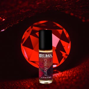 May include: A roll-on perfume bottle with a black cap and a label that reads "ruby red." The bottle is .17 fl oz (5 ml). The background features a large, faceted red gemstone and a dark red, textured surface.