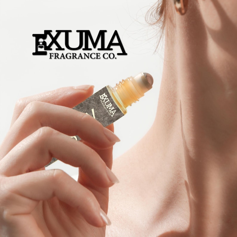 Puede incluir: Un frasco de perfume roll-on sostenido en una mano. El frasco contiene un l&iacute;quido de color dorado. La etiqueta dice "EXUMA FRAGRANCE CO." en texto negro. El roll-on es de color marr&oacute;n claro. Perfume.