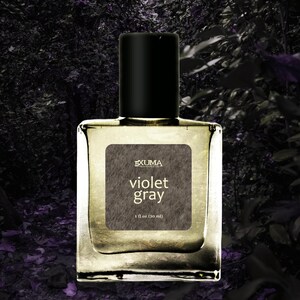 Puede incluir: Botella de perfume cuadrada y transparente con tap&oacute;n negro. La etiqueta gris dice "Violet Gray" y "1 fl oz (30 ml)". El fondo es una imagen oscura y borrosa de follaje. Contiene 30 ml.