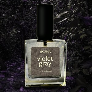 Puede incluir: Botella de perfume de vidrio transparente con tapa negra. La etiqueta dice "EXUMA FRAGRANCE CO." y "violet gray". La botella contiene 50 ml de perfume. El fondo es un bosque oscuro y borroso.