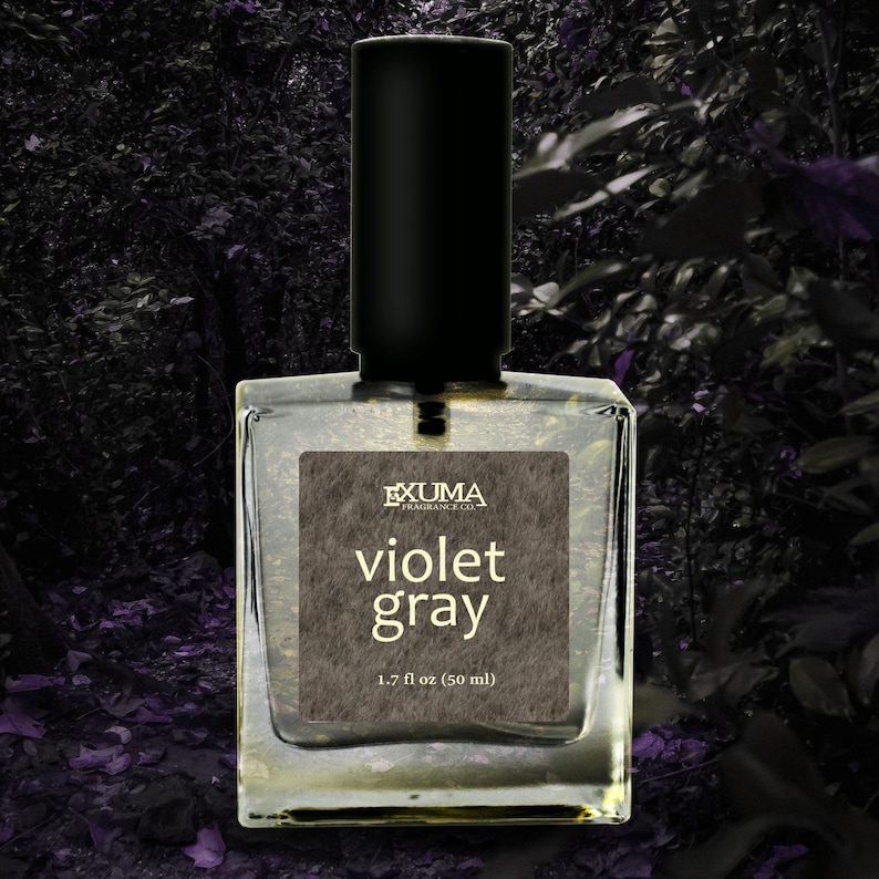 Puede incluir: Botella de perfume de vidrio transparente con tapa negra. La etiqueta dice "EXUMA FRAGRANCE CO." y "violet gray". La botella contiene 50 ml de perfume. El fondo es un bosque oscuro y borroso.