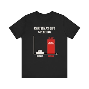Peut inclure: Un t-shirt noir à manches courtes avec un graphique blanc représentant un diagramme en barres intitulé CHRISTMAS GIFT SPENDING. Il montre une petite barre blanche étiquetée $200 BUDGET et une grande barre rouge $1,847 ACTUAL avec WE DON'T TALK ABOUT IT.