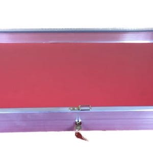 May include: A rectangular display case with a silver metal frame and a red interior. The case has a hinged lid with a lock and key. The display case is designed to showcase jewelry, collectibles, or other items.