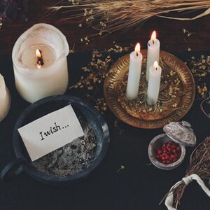 May include: A dark wooden surface with three white candles, a small bowl of red berries, a note that says "I wish..." and a small brass tray with a decorative design.
