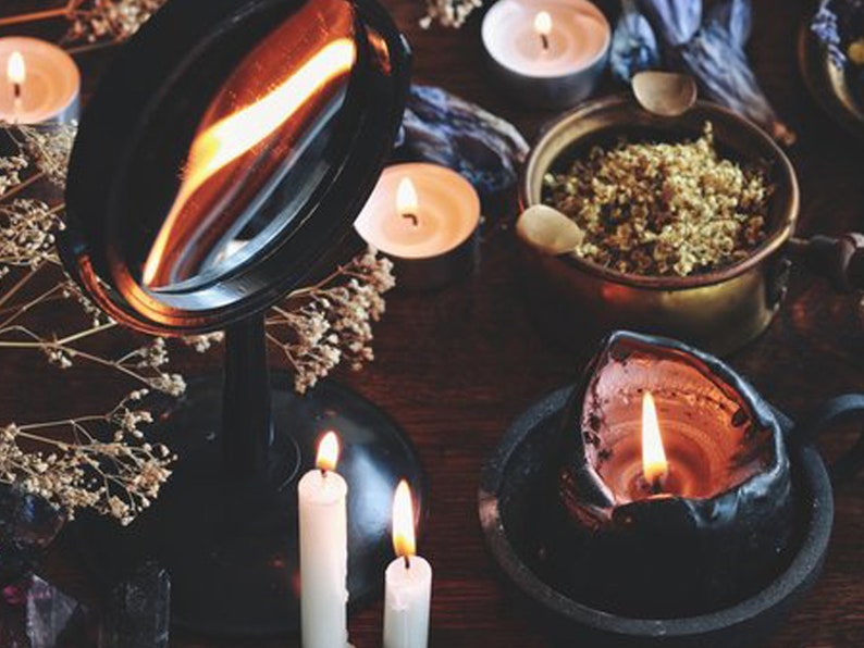 May include: A black vanity mirror with a silver reflective surface, surrounded by candles and dried flowers. The candles are lit and casting a warm glow.
