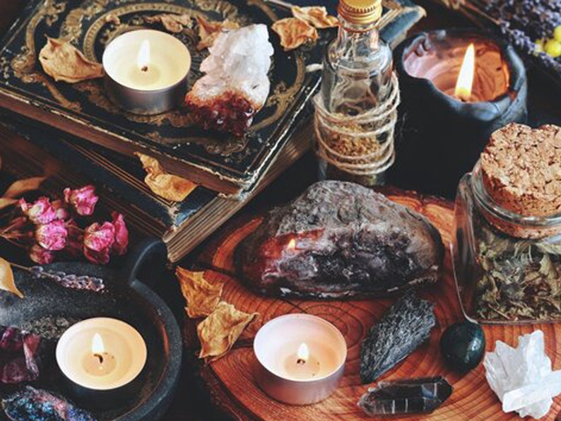 May include: A collection of items for spell casting, including candles, crystals, herbs, and a book. The items are arranged on a wooden surface with a dark background.