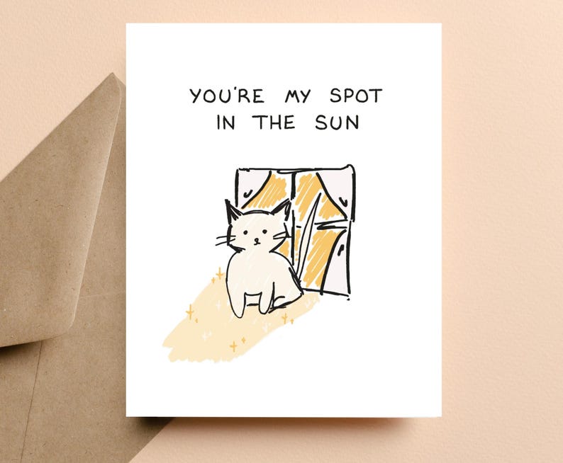 May include: A white greeting card with the text "YOU'RE MY SPOT IN THE SUN" above a sketched illustration of a white cat sitting by a window. The window has yellow curtains and the cat is in a patch of yellow sunlight.