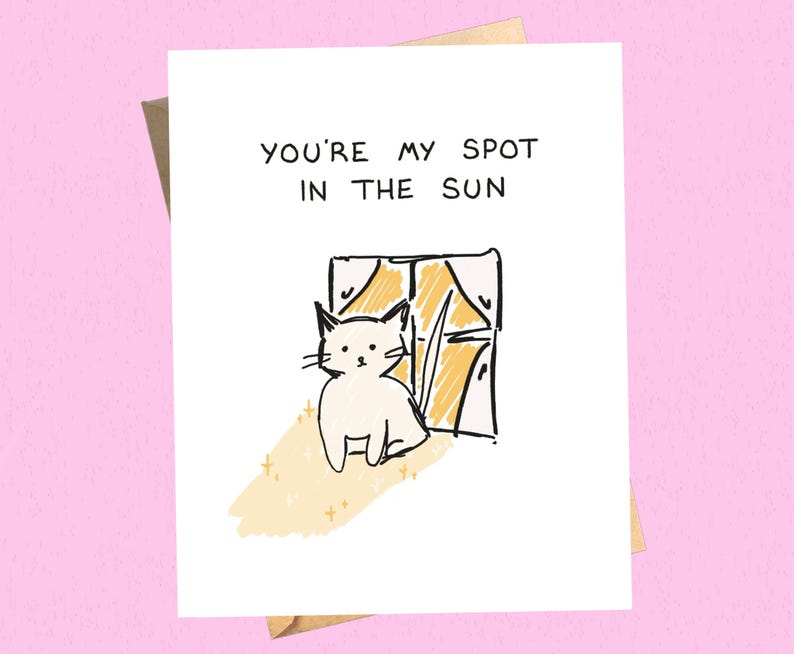 May include: A greeting card with the text "YOU'RE MY SPOT IN THE SUN" above a drawing of a white cat sitting by a window. The window is drawn with yellow and black lines, and the cat is drawn with black lines.