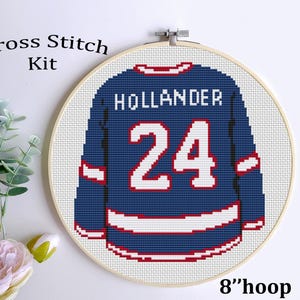 May include: Cross stitch kit featuring a hockey jersey design. The jersey is navy blue with white and red accents, displaying the name "HOLLANDER" and the number "24". The design is set in an 8-inch hoop.