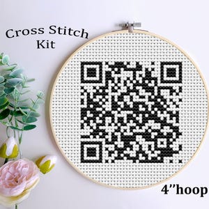Könnte beinhalten: Ein Kreuzstich-Set mit einem schwarz-weißen QR-Code-Design, das in einem 10 cm-Reifen angebracht ist. Die Worte "Cross Stitch Kit" stehen über dem Reifen. Links befindet sich ein Blumen- und Grünstrauß.