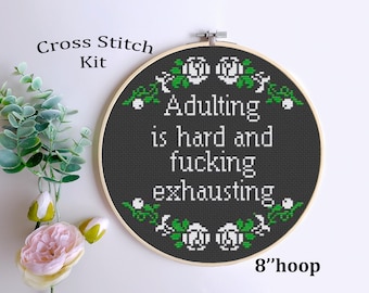 May include: Cross stitch kit featuring a black embroidery hoop with white flowers and green leaves. The text reads "Adulting is hard and fucking exhausting". The hoop is 8 inches in diameter.