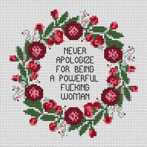 May include: Cross-stitch design featuring a floral wreath with red and pink flowers and green leaves. The text in the center reads "NEVER APOLOGIZE FOR BEING A POWERFUL FUCKING WOMAN."