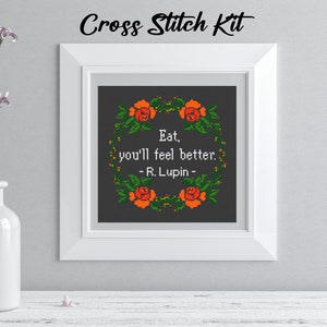 Pu&ograve; includere: Kit per punto croce incorniciato con la frase "Eat, you'll feel better. - R. Lupin -" circondata da una ghirlanda floreale. Il kit &egrave; in una cornice bianca, con il testo "Cross Stitch Kit" in alto.