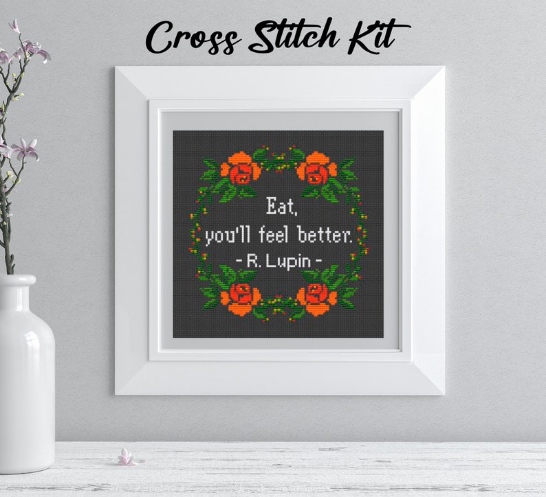 Pu&ograve; includere: Kit per punto croce con un design incorniciato. Il design presenta la citazione "Eat, you'll feel better. - R. Lupin -" circondata da una ghirlanda di rose arancioni e foglie verdi. Il testo "Cross Stitch Kit" &egrave; in alto.