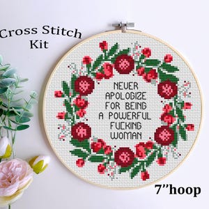 May include: Cross stitch kit with a floral wreath design. The embroidery hoop is 7 inches in diameter. The text reads: "NEVER APOLOGIZE FOR BEING A POWERFUL FUCKING WOMAN". The wreath features red flowers and green leaves.