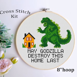 May include: Cross stitch kit featuring a green Godzilla monster and a yellow house with the text "May Godzilla Destroy This Home Last" on a white background. The kit is in an 8-inch hoop.